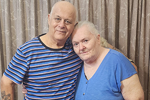 An older man and woman stand side-by-side with their arms around each other