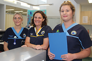 Three female nurses wearing Rockingham General Hospital uniforms stand beside a counter