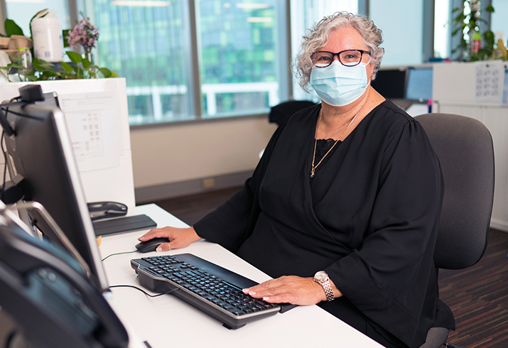 A woman wearing a surgical mask sits in front of the keyboard and computer.