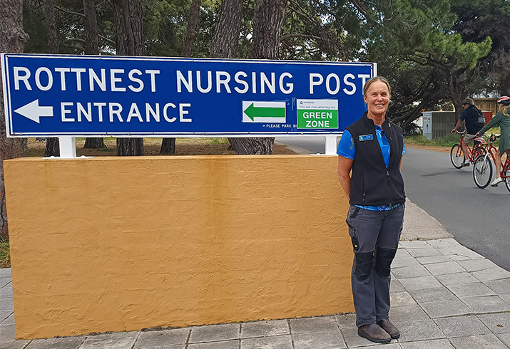 A female nurse stands beside a roadside sign that reads Rottnest Nursing Post Entrance