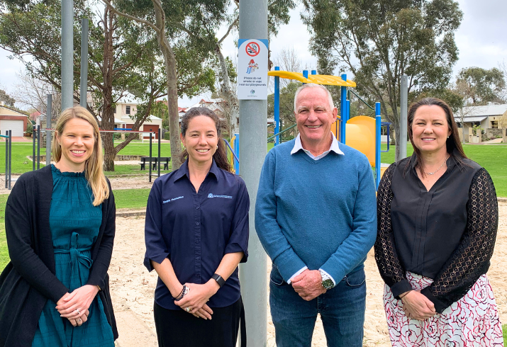 Four staff from SMHS Health Promotion and the Town of East Fremantle standing in front of a playground, with the new smoke-free signage visible behind them.