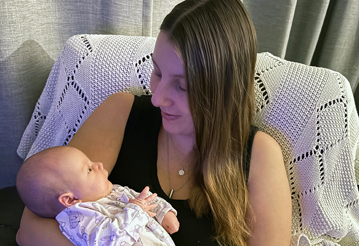 A woman sits on a chair cradling a newborn baby.