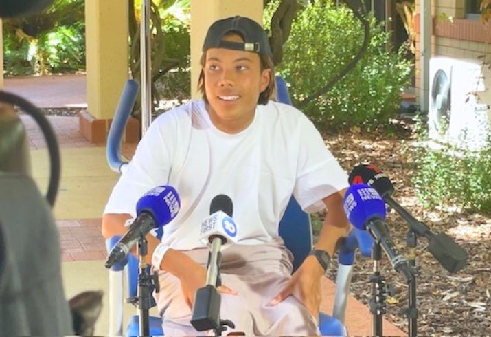 Zac Hlaing sitting in a wheelchair with microphones in front of him talking to the media.