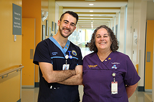 A male nurse and a female nurse stand in a hospital corridor