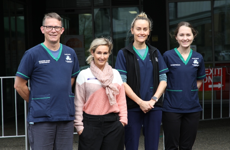 A male and three female health professionals stand together outside a building.