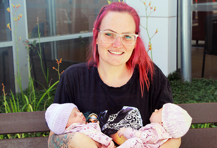 A young woman holds two newborn baby twins