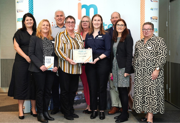 Nine members of the SMHS Health Promotion team standing together smiling, with two holding the award certificate in the middle. 