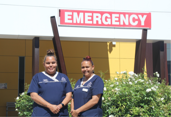 Aboriginal Health Practitioners Emily and Danielle standing together outside with the emergency department sign in the background.
