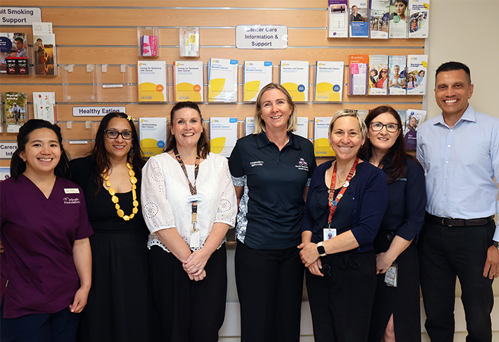Seven representatives of the Rockingham Peel Group Integrated Cancer Service, South Metropolitan Health Service Health Promotion and local government stand together in front of a variety of health promotion resources